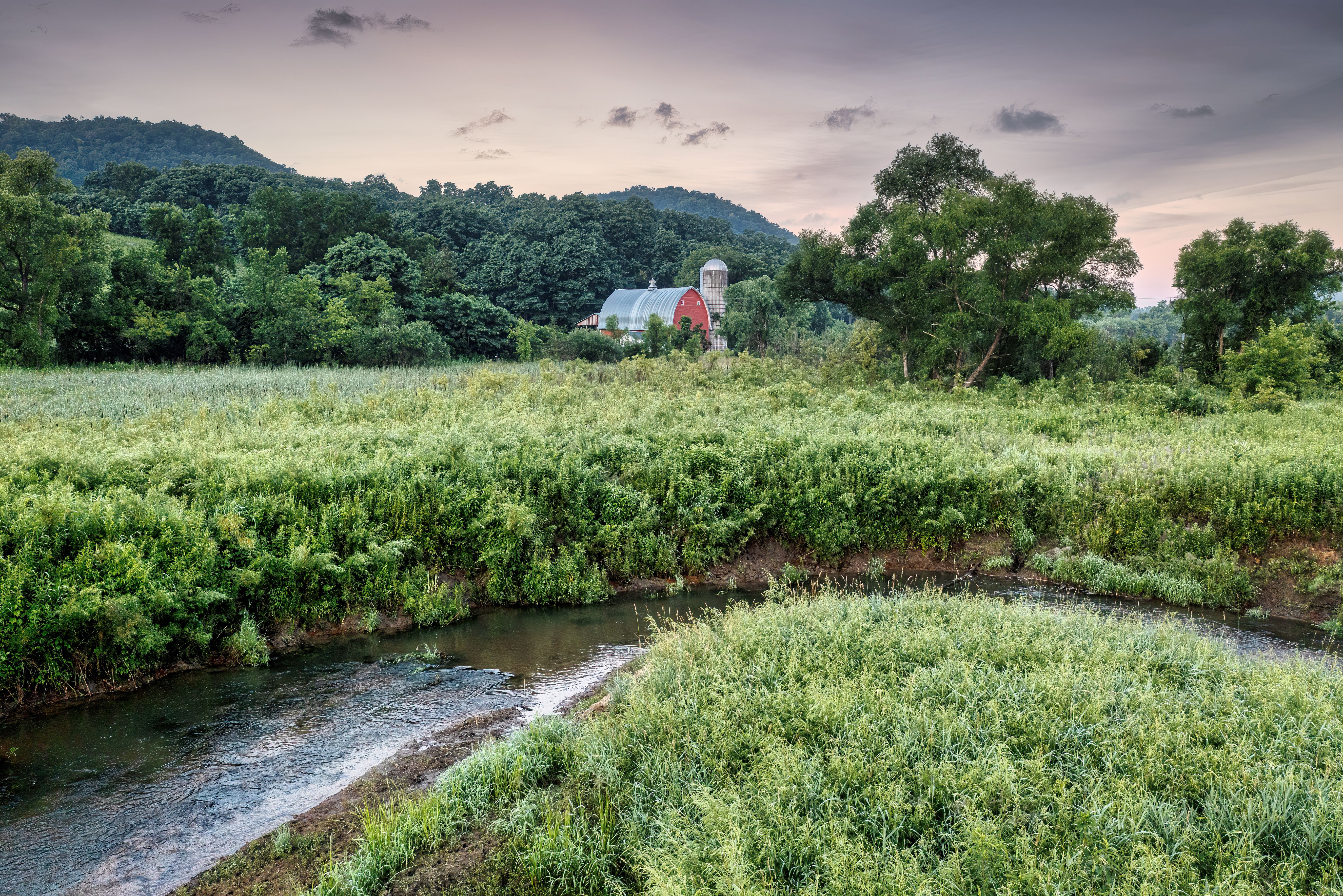A red barn and silo above a creek running through a green valley